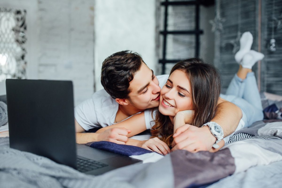 счастливая молодая пара лежит дома на кровати и пользуется ноутбуком