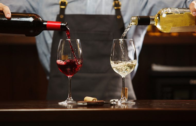 Сомелье-мужчина наливает красное и белое вино в бокалы на длинной ножке