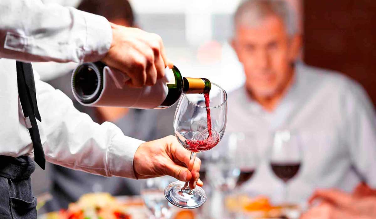 Официант наливает красное вино посетителям
